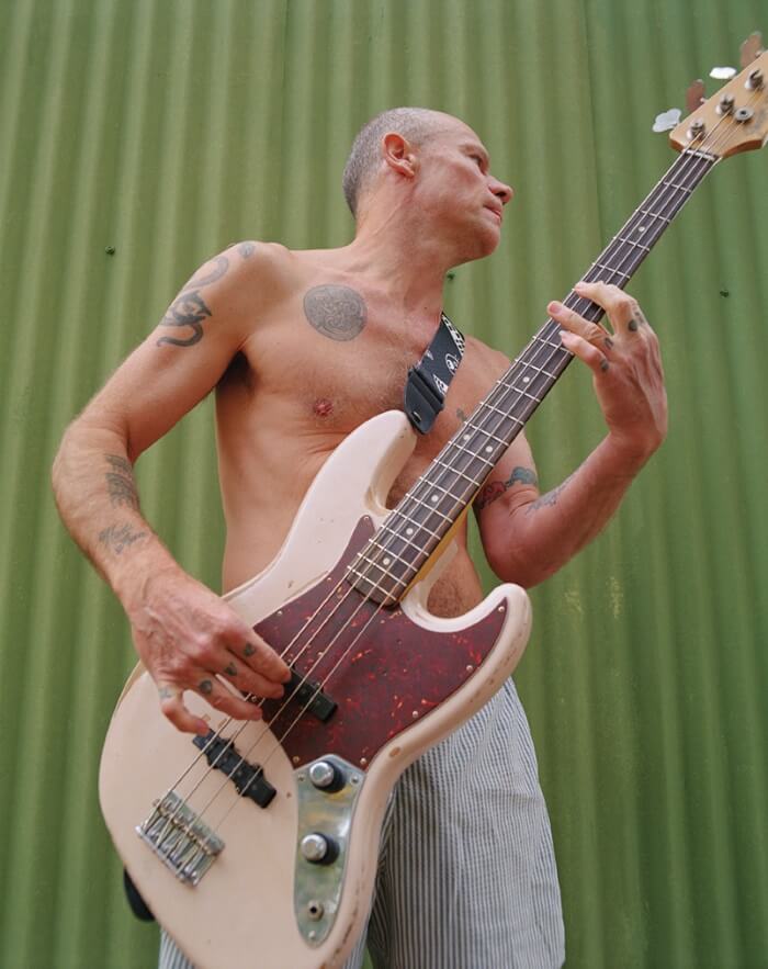 Flea, baixista do Red Hot Chilli Peppers, com seu baixo 4 cordas Fender Jazz Bass 61'. No fundo uma superfície verde. 